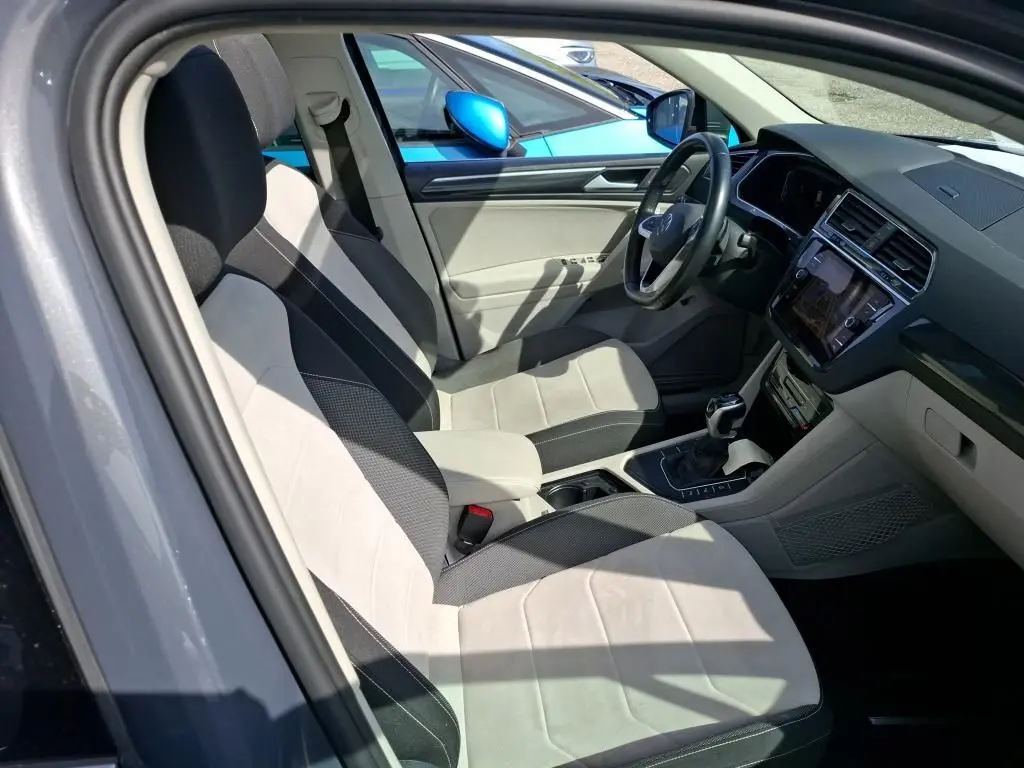 Vue intérieure côté conducteur du Volkswagen Tiguan gris 2023, sièges tissu clair et tableau de bord moderne avec écran tactile.