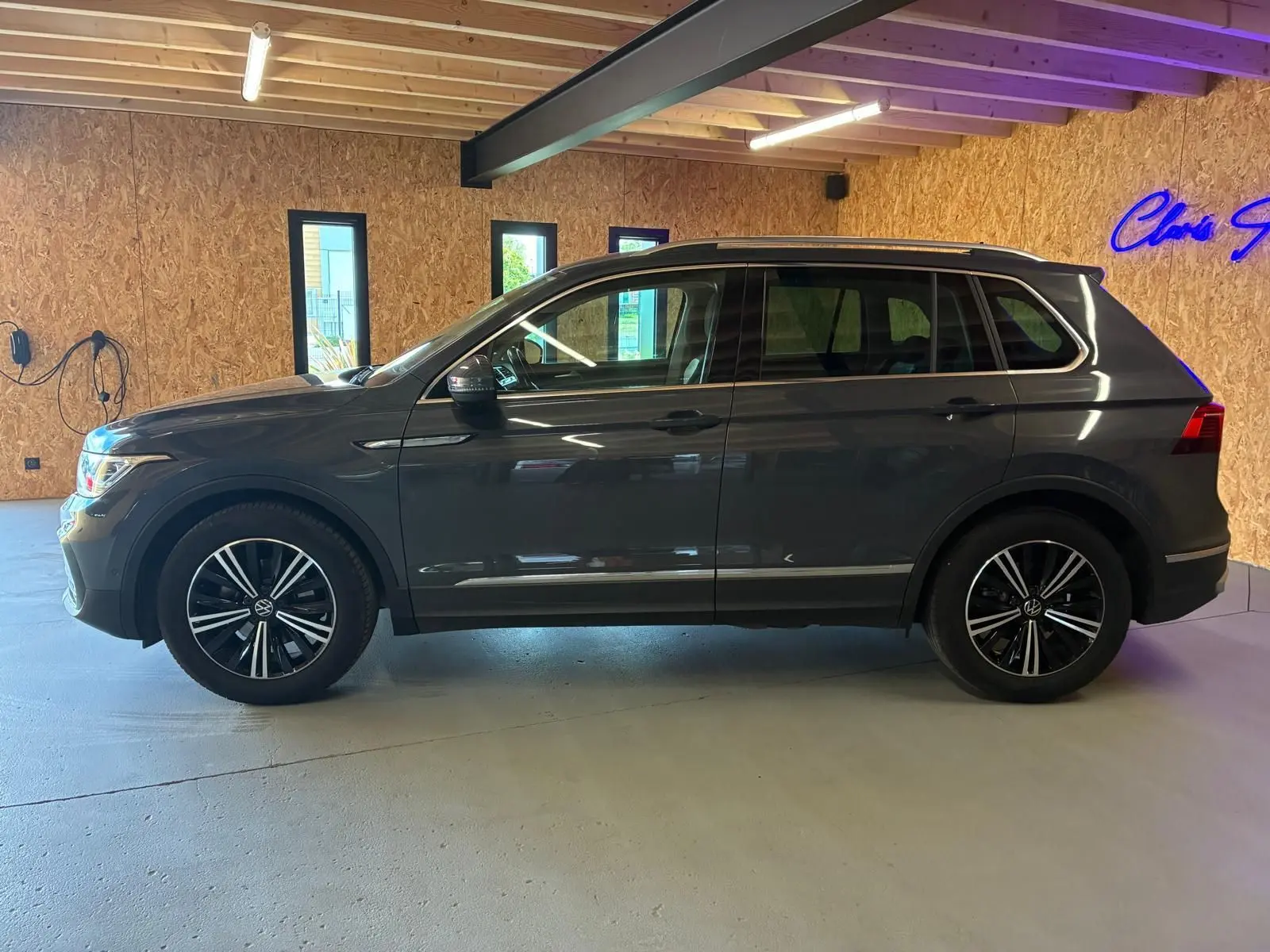 Vue de profil côté gauche d'un Volkswagen Tiguan gris 2023 avec jantes alliage et toit ouvrant panoramique visible.