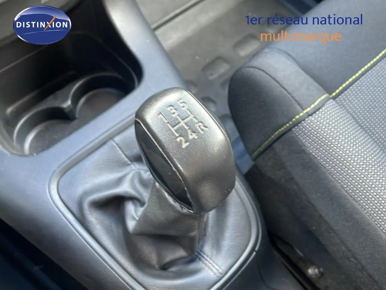 Gros plan sur le levier de vitesses manuel noir et la sellerie tissu gris avec surpiqûres jaunes d'une Citroën C3 blanche.