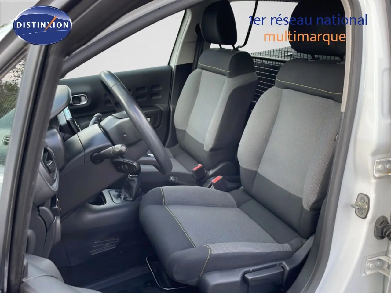 Vue intérieure côté conducteur de la Citroën C3 Société blanche, sièges tissu gris avec surpiqûres jaunes visibles.