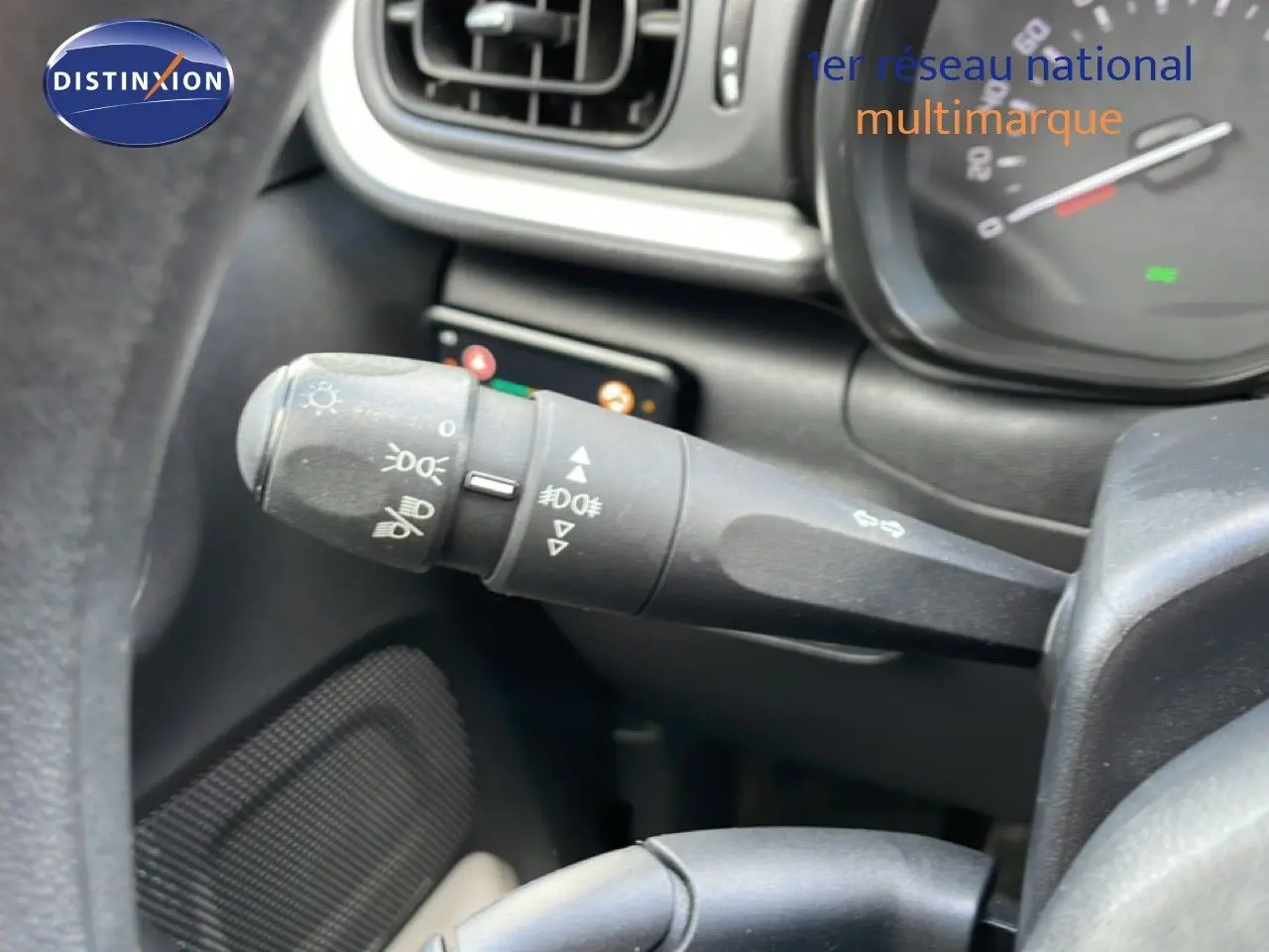 Gros plan sur la commande des phares et clignotants à gauche du volant dans l’habitacle d’une Citroën C3 blanche.