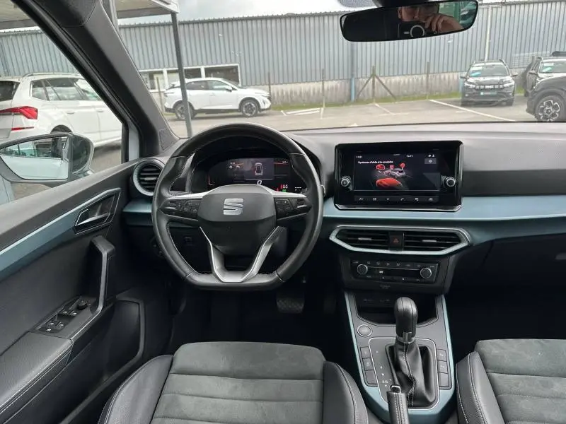 Vue intérieure avant du SEAT Arona 2025 avec tableau de bord noir, volant cuir multifonction et écran tactile central.