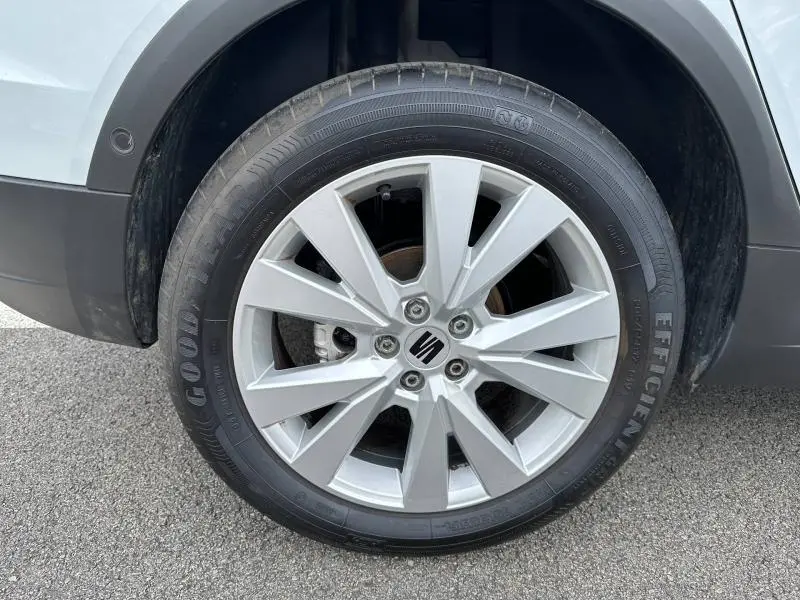 Gros plan sur la jante alu argentée avec logo SEAT d'une SEAT Arona blanche, vue côté gauche arrière.