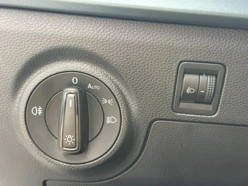 Gros plan sur la molette de réglage des phares et le variateur d'intensité lumineuse du tableau de bord noir du SEAT Arona blanc.