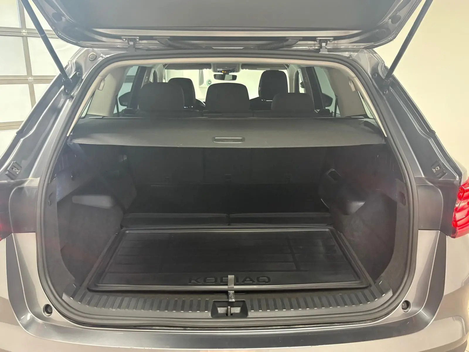 Coffre ouvert vu de l'arrière d'un Skoda Kodiaq gris graphite 2025, avec tapis de coffre marqué KODIAQ.