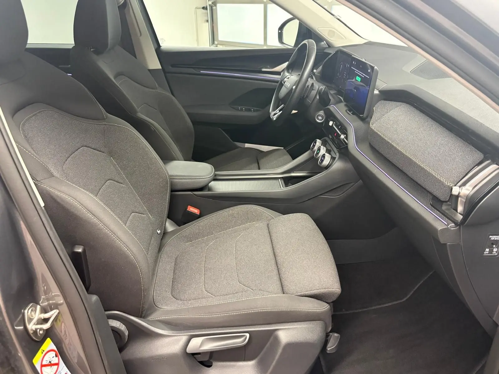 Intérieur côté conducteur du Skoda Kodiaq 2025 gris graphite, avec sièges tissu et tableau de bord moderne équipé d’un écran tactile.