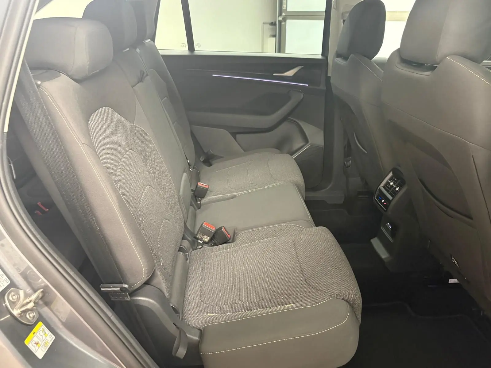 Vue intérieure côté gauche des sièges arrière gris foncé du Skoda Kodiaq 2025 avec éclairage d'ambiance violet sur la porte.