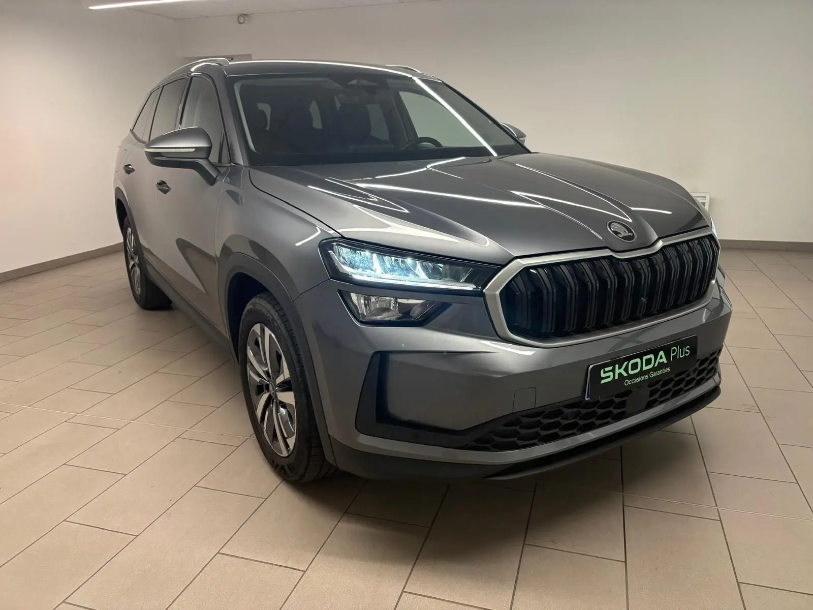 Vue 3/4 avant droite du Skoda Kodiaq gris graphite 2025 avec calandre noire et phares LED allumés.