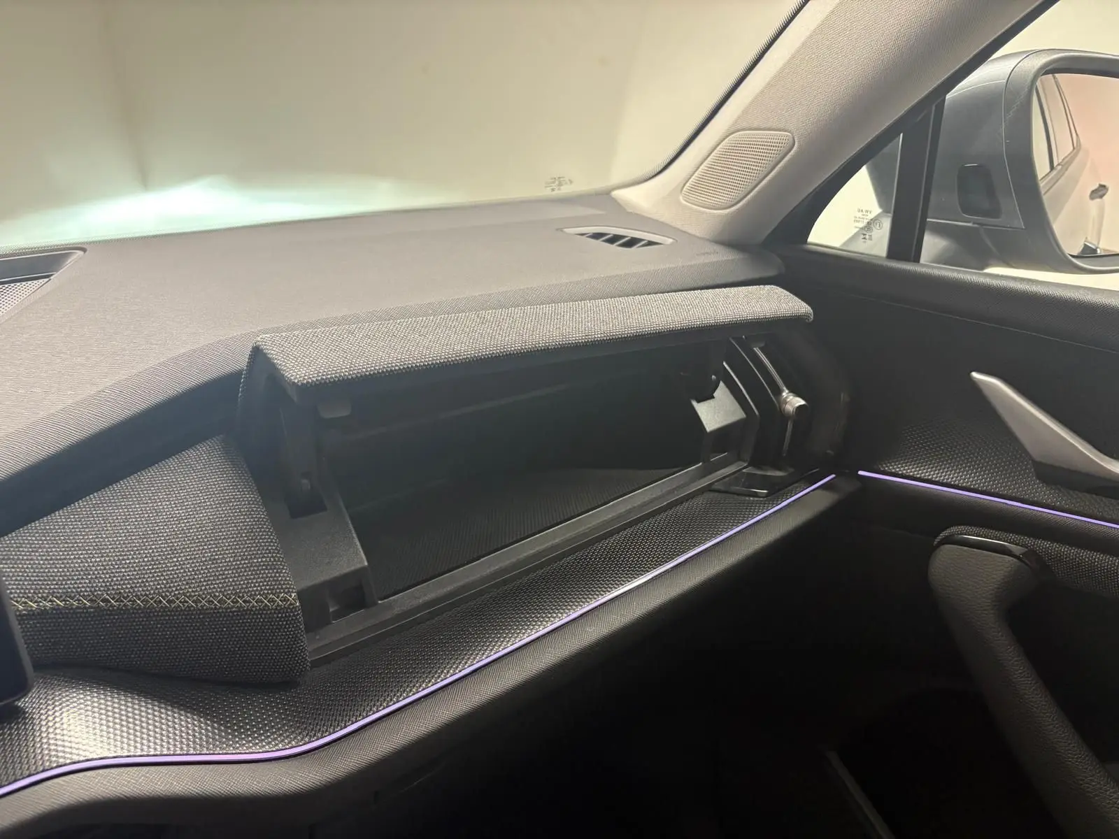 Intérieur du Skoda Kodiaq 2025 côté passager, tableau de bord gris avec boîte à gants ouverte et éclairage d'ambiance violet.