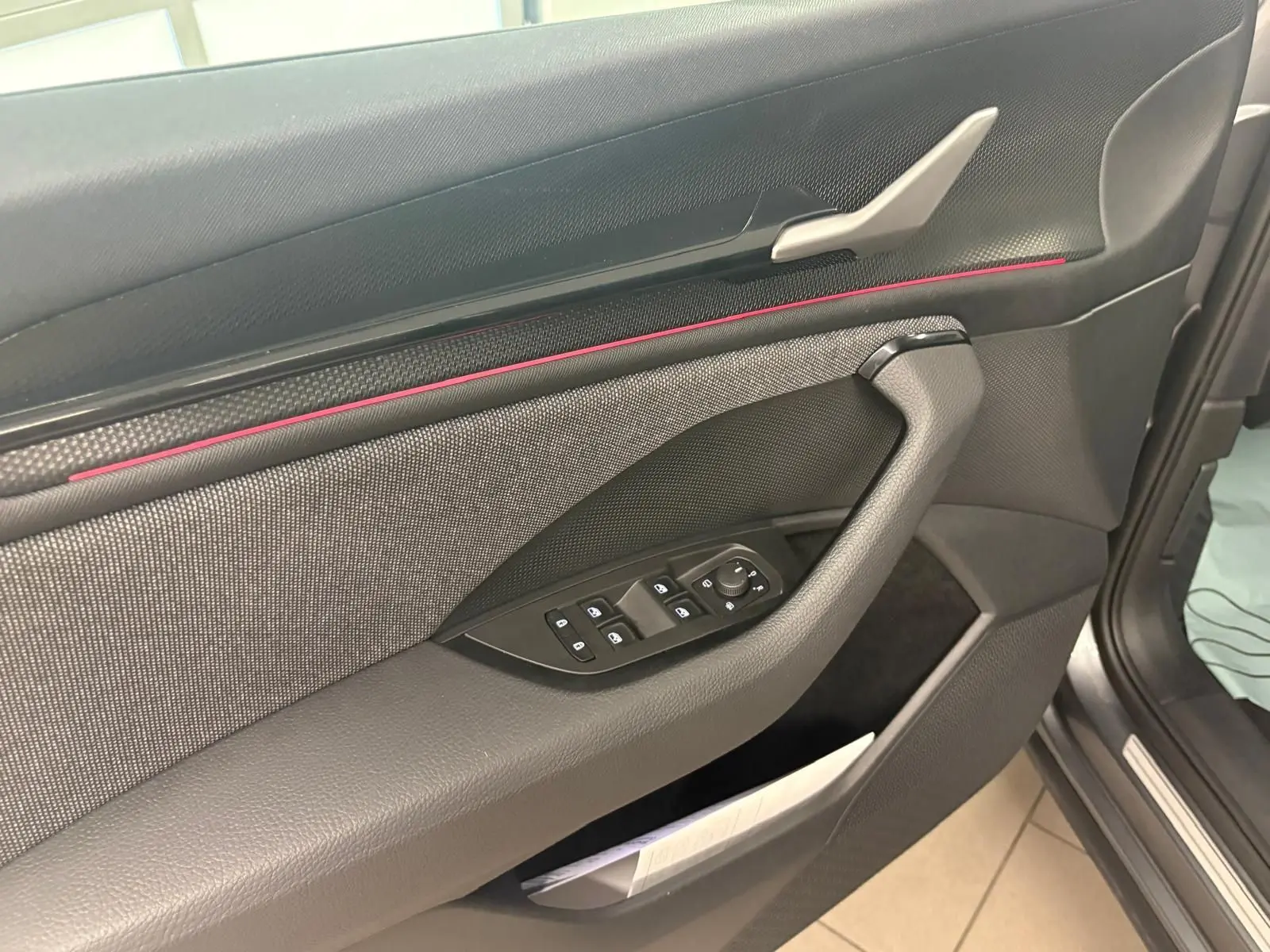 Détail de la porte côté conducteur du Skoda Kodiaq 2025 gris graphite, avec commandes électriques et bande décorative rouge.