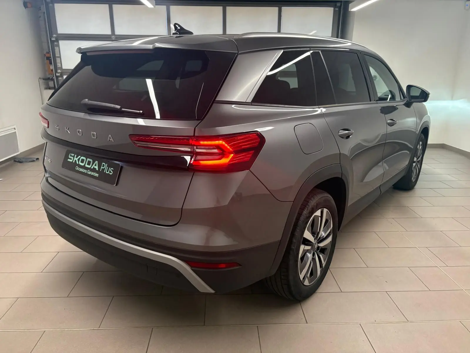 Vue 3/4 arrière droite du Skoda Kodiaq gris graphite 2025 avec feux arrière allumés dans un showroom.