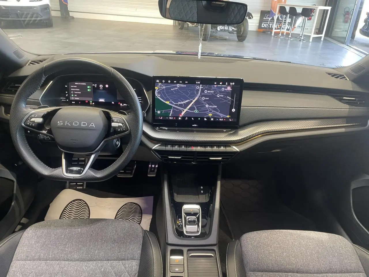 Vue intérieure avant de la Skoda Octavia 2025 Sportline, tableau de bord noir avec écran tactile central et volant cuir.