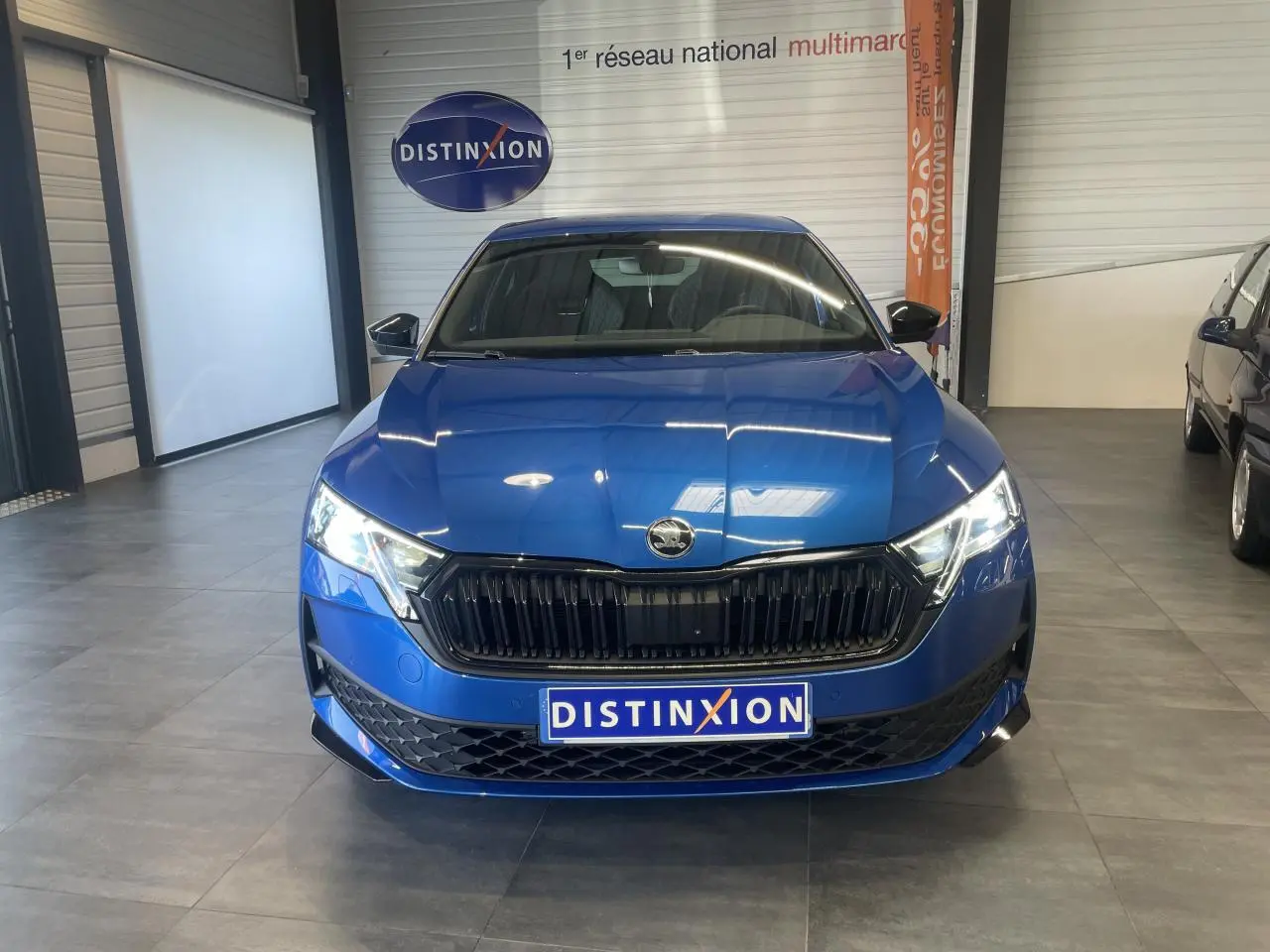 Vue avant d'une Skoda Octavia Sportline bleu foncé avec calandre noire et phares allumés en showroom.