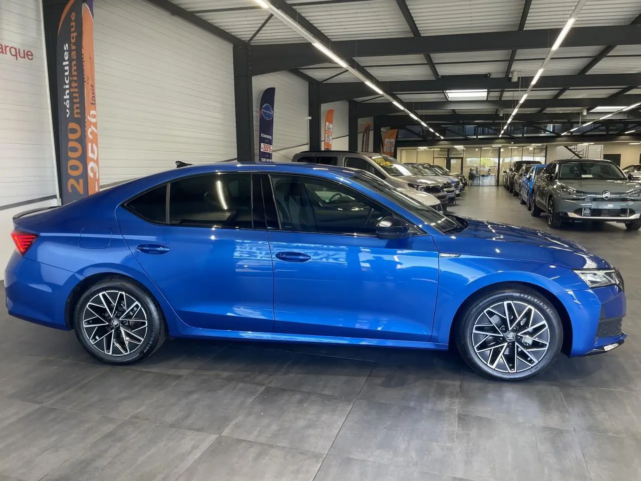 Vue latérale droite d'une Skoda Octavia 2025 bleu foncé avec jantes alliage noires et vitres teintées en showroom.