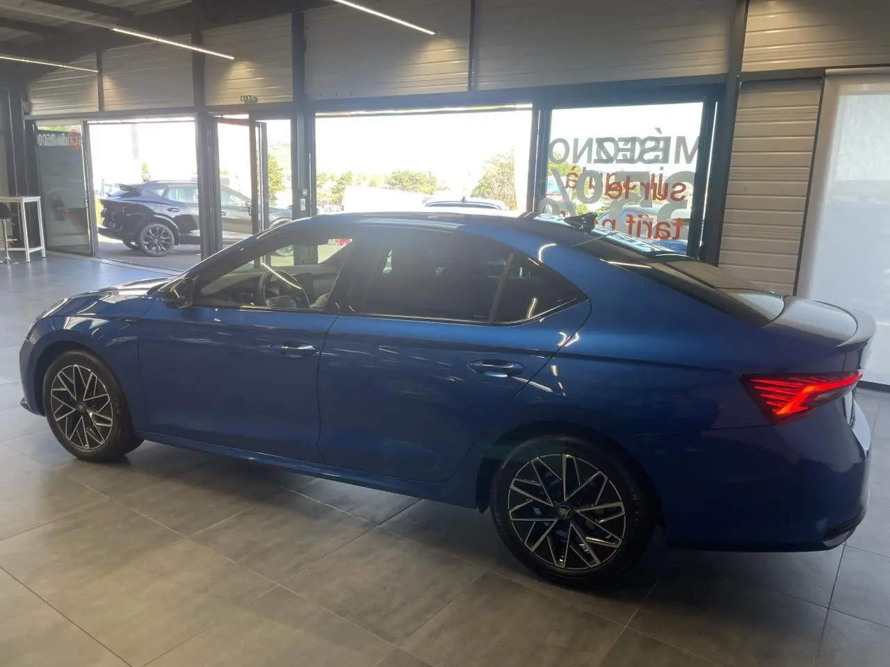 Vue latérale gauche d'une Skoda Octavia 2025 bleu foncé avec jantes alliage noires et feux arrière LED allumés.