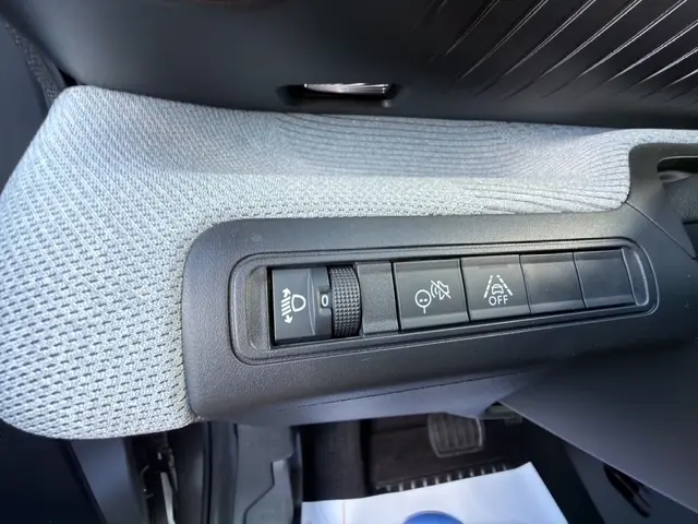 Gros plan sur les commandes de réglage des phares et aides à la conduite du côté gauche intérieur d’un Citroën C3 Aircross gris foncé.