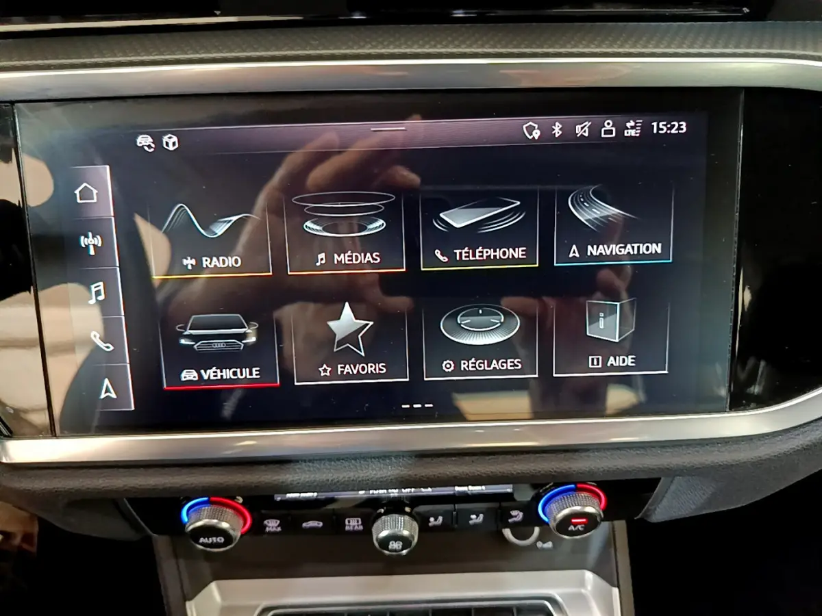 Écran tactile central de l'Audi Q3 noir, vue rapprochée du tableau de bord avec commandes climatisation visibles.