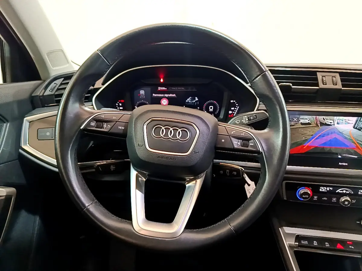 Vue intérieure centrée sur le volant cuir noir de l'Audi Q3 35 TDI 2021 avec tableau de bord digital et écran tactile.