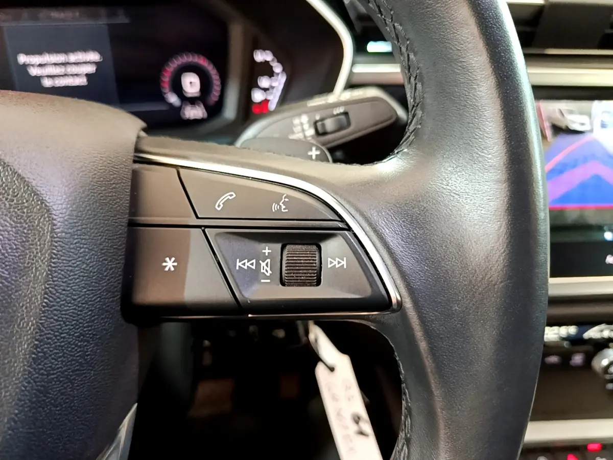 Gros plan sur les commandes gauche du volant cuir noir de l'Audi Q3 35 TDI 2021 avec écran de caméra de recul visible.