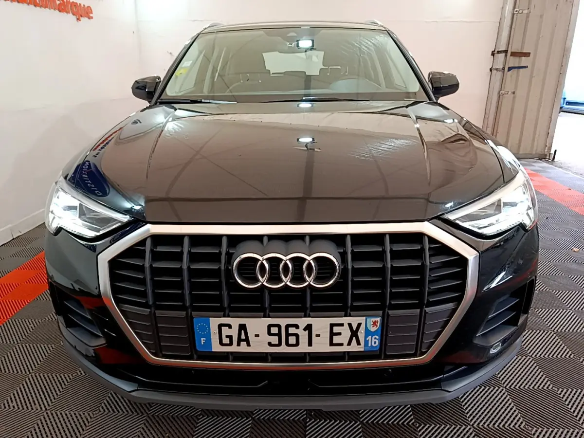 Vue frontale d'un Audi Q3 noir 2021 avec calandre hexagonale et phares LED allumés dans un garage.