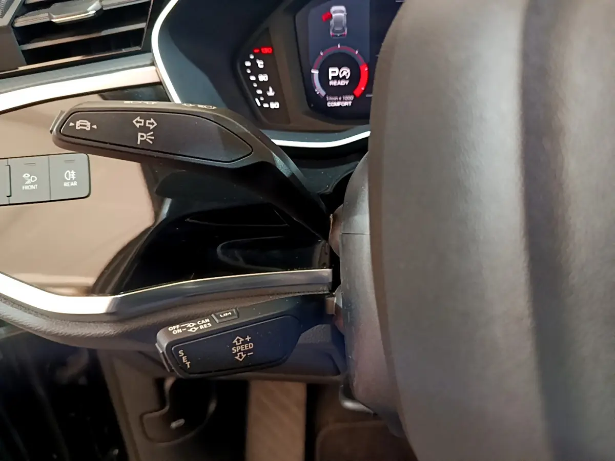 Vue rapprochée du levier de commande multifonctions côté gauche du volant d’un Audi Q3 noir, tableau de bord digital visible.