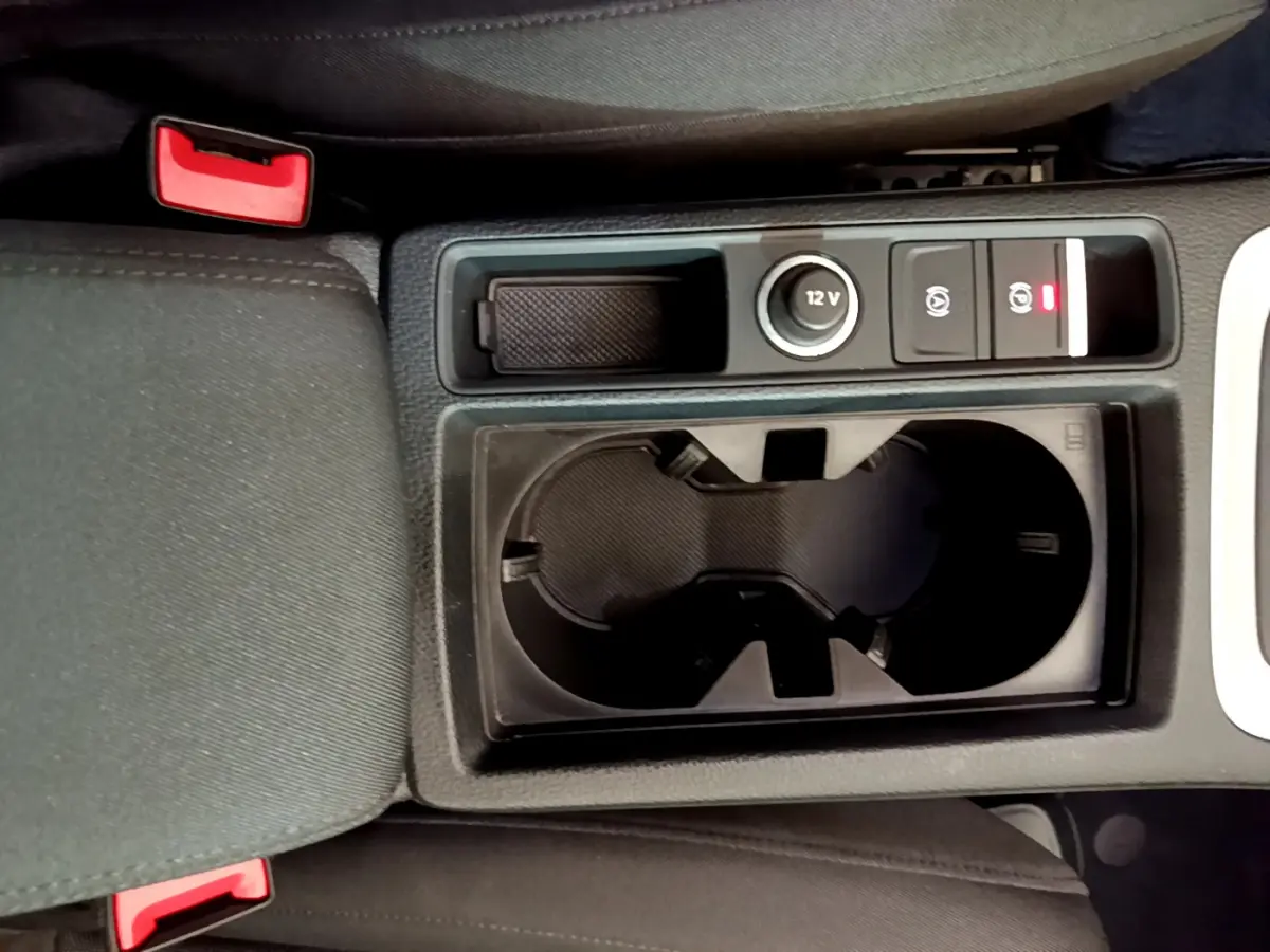 Vue plongeante sur la console centrale noire de l'Audi Q3 35 TDI 150 S tronic avec porte-gobelets et bouton 12V.