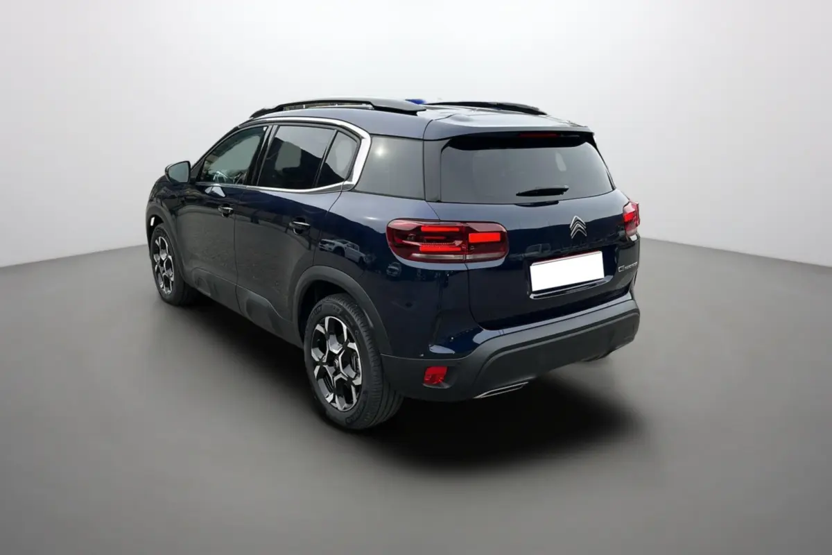 Vue 3/4 arrière gauche du Citroën C5 Aircross Hybrid 145 en Eclipse Blue avec barres de toit et jantes alu 18 pouces.