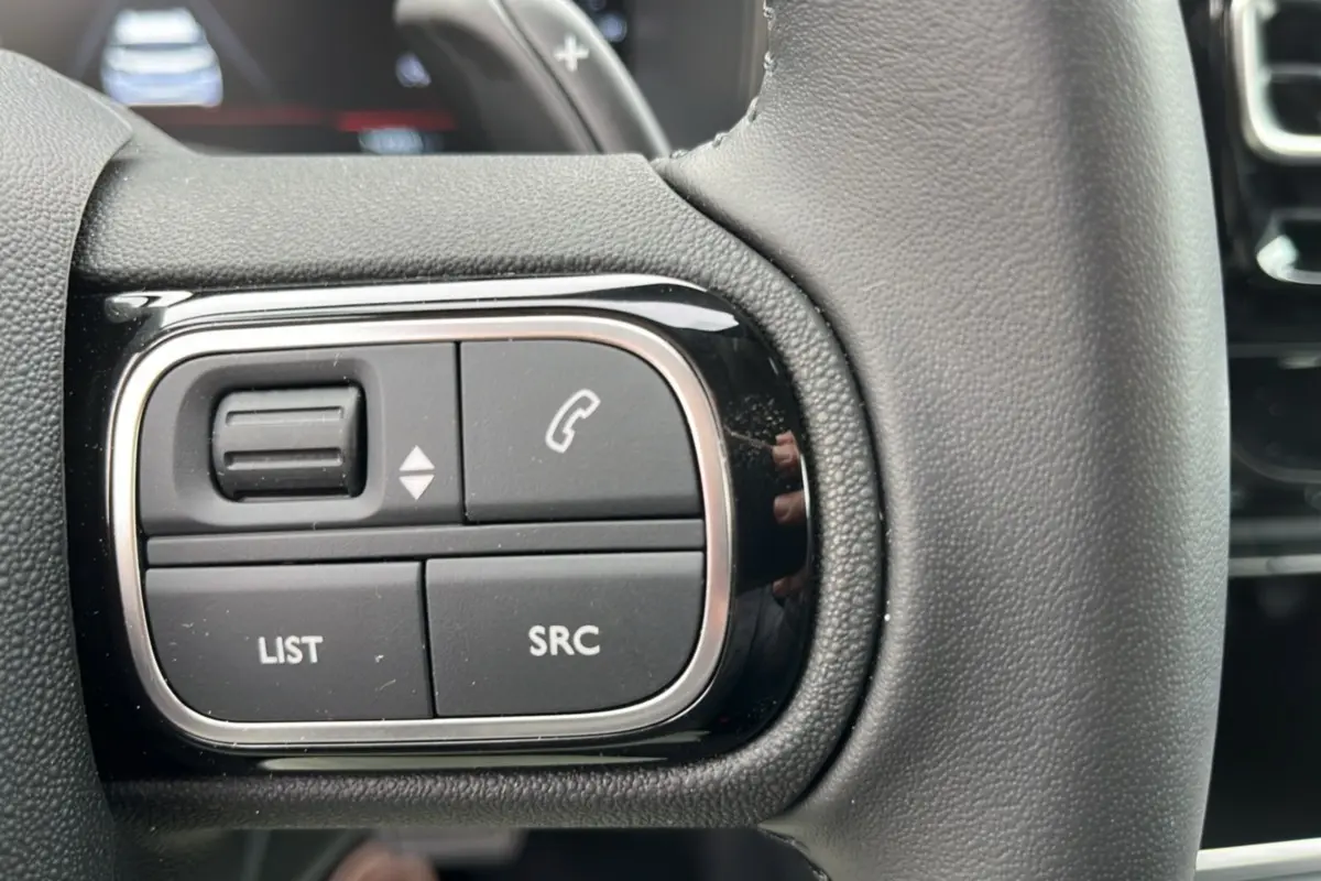 Gros plan sur les commandes gauche du volant cuir multifonctions du Citroën C5 Aircross Hybrid 145 en noir.