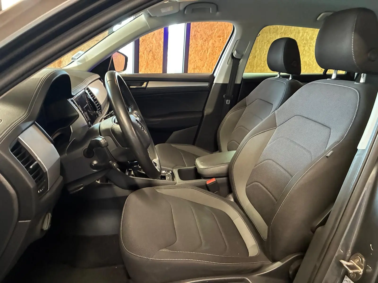 Vue intérieure côté conducteur du Skoda Kodiaq 2023, sièges tissu gris et tableau de bord avec volant cuir.