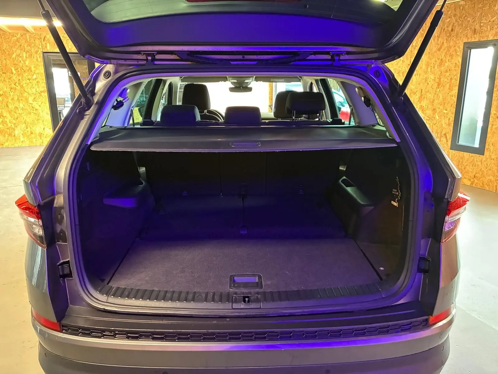 Coffre ouvert vu de l'arrière d'un Skoda Kodiaq gris, montrant l'espace de chargement et la tablette cache-bagages.
