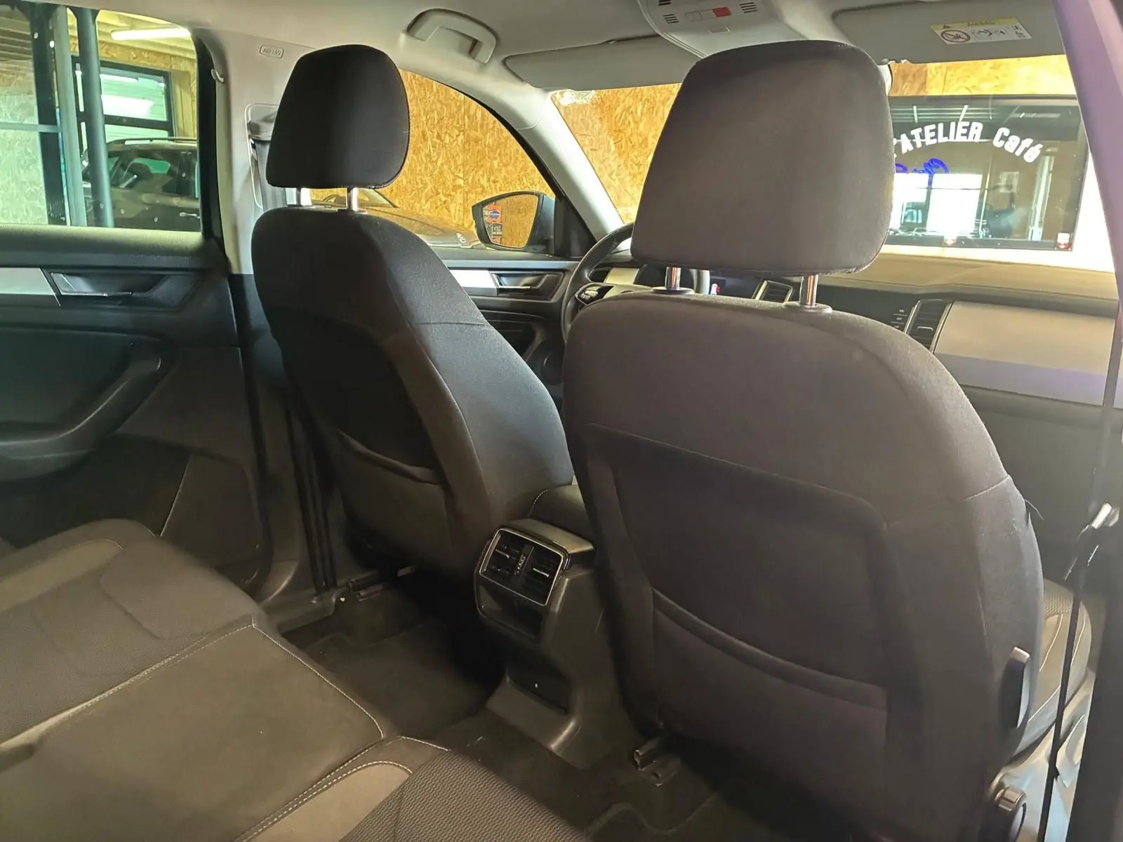 Vue intérieure arrière du Skoda Kodiaq gris 7 places, montrant les sièges avant en tissu noir et la console centrale avec aérateurs.