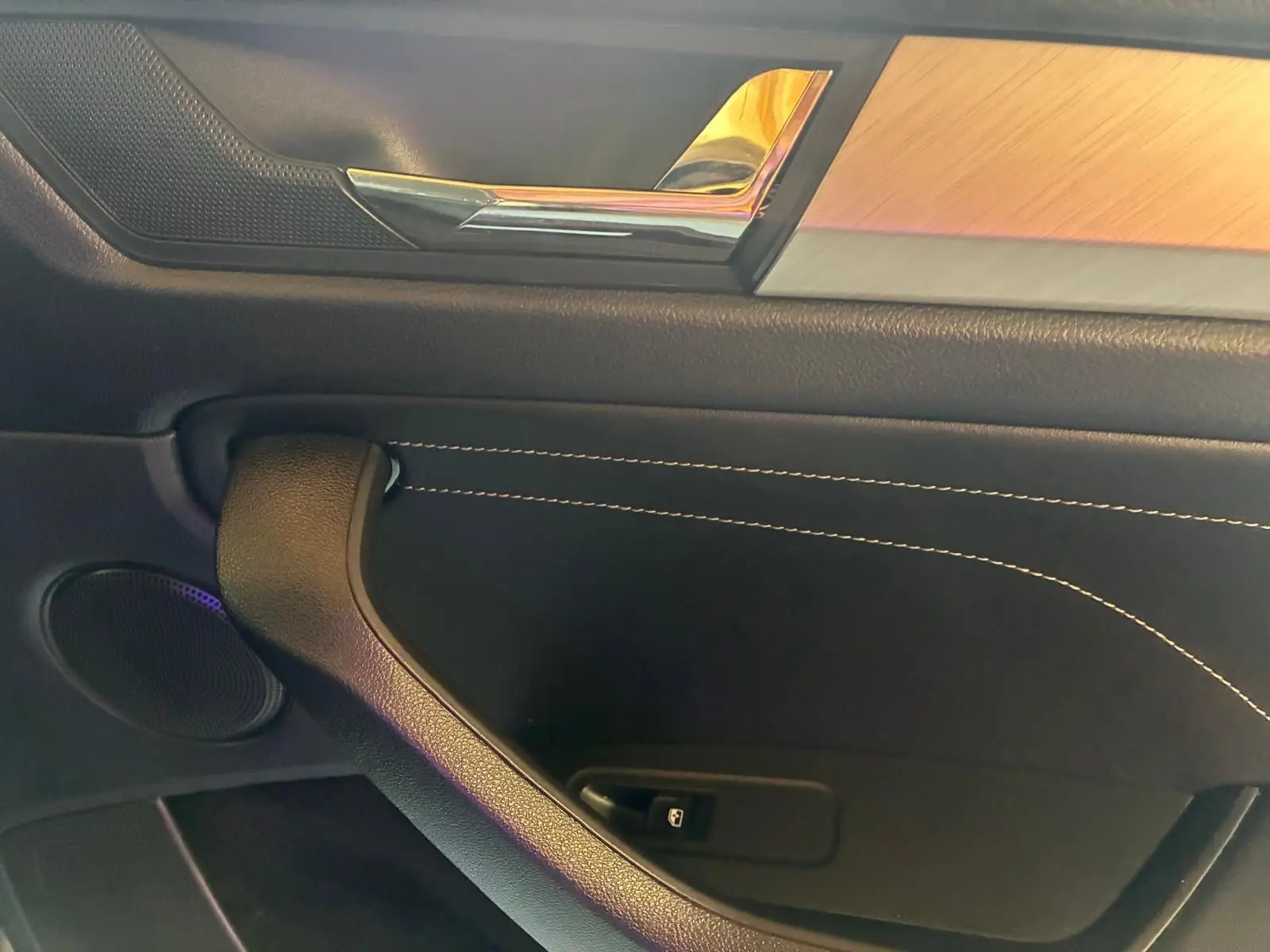 Détail de la porte intérieure côté gauche d’un Skoda Kodiaq gris, avec insert bois et surpiqûres blanches.