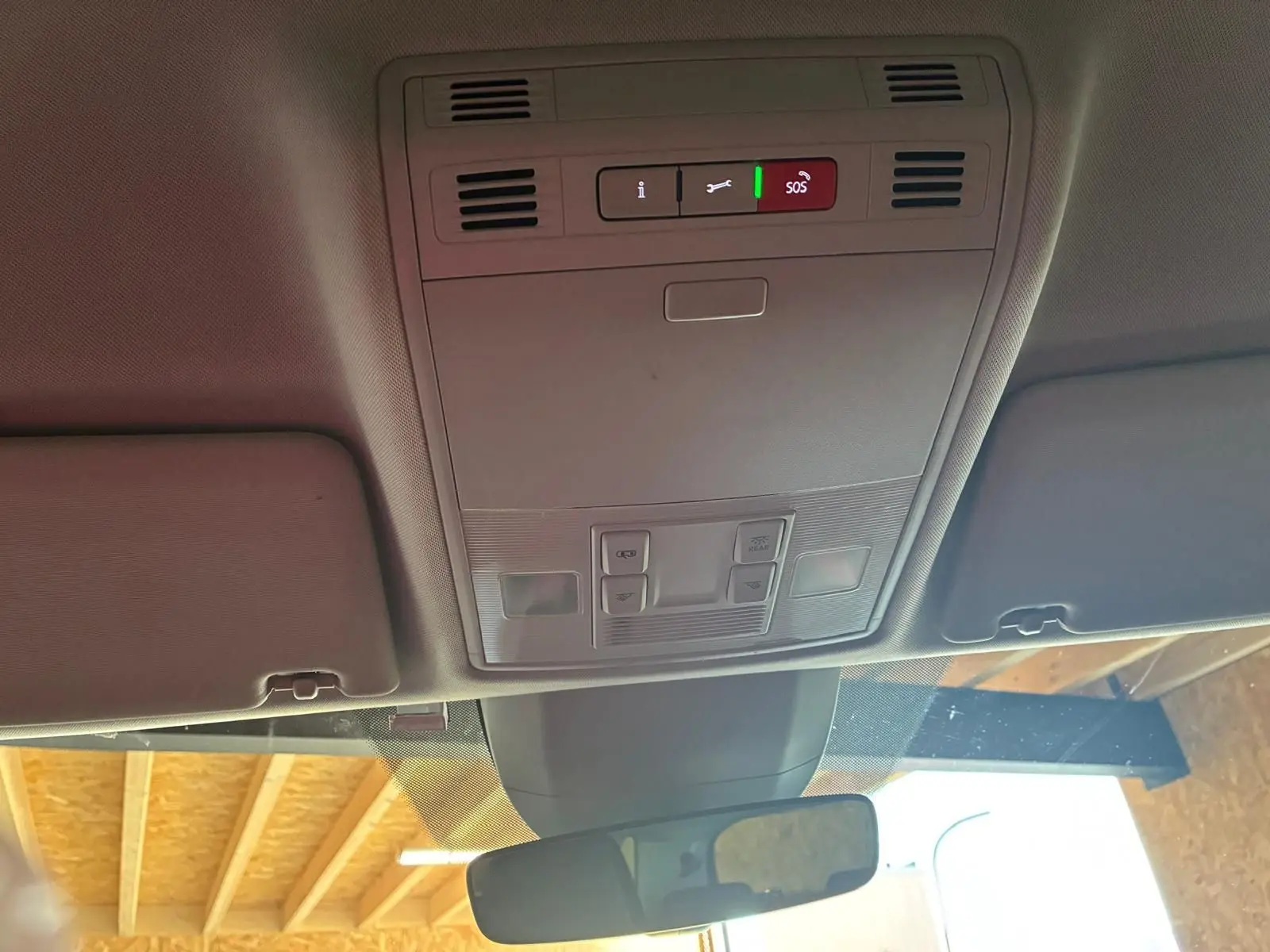 Vue intérieure du plafond avant du Skoda Kodiaq gris, montrant les commandes d'éclairage et le bouton SOS au centre.