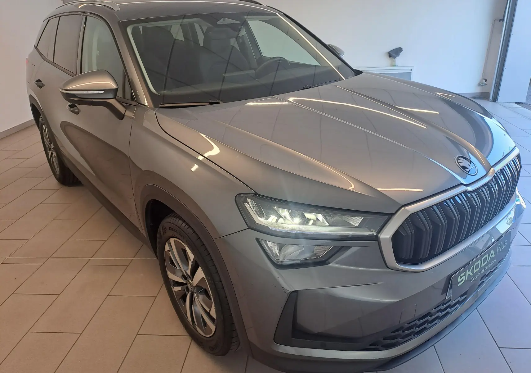Vue 3/4 avant droite du Skoda Kodiaq gris graphite 2025 avec calandre marquée et phares LED allumés.