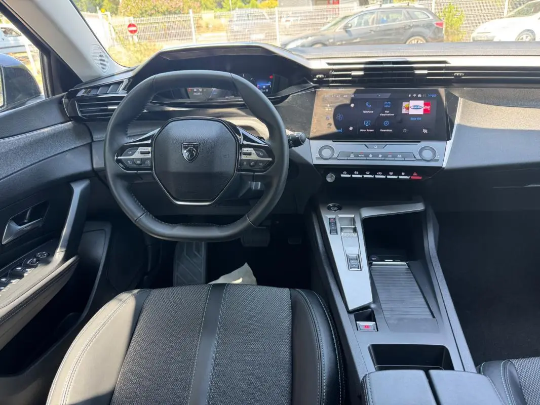Vue intérieure avant de la Peugeot 308 gris, avec volant multifonction, écran tactile et console centrale moderne.
