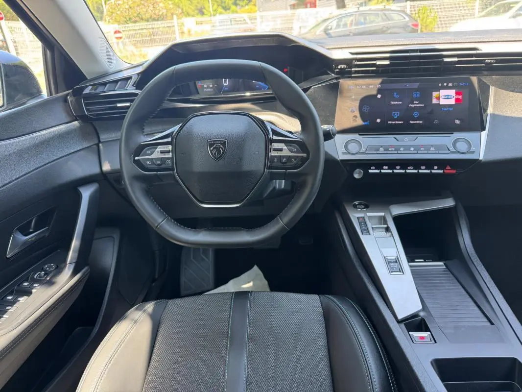 Vue intérieure de face du poste de conduite gris de la Peugeot 308 2025 avec volant multifonction et écran tactile central.