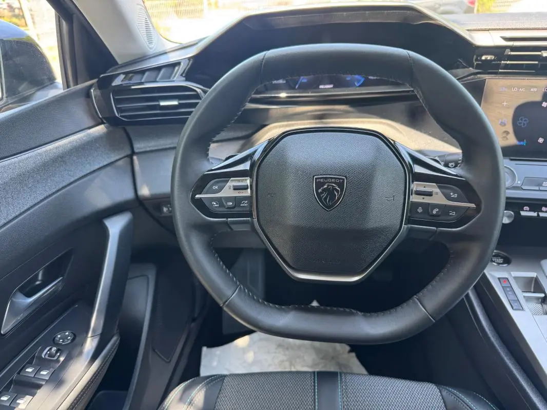 Vue intérieure centrée sur le volant noir de la Peugeot 308 2025 avec commandes intégrées et tableau de bord numérique.