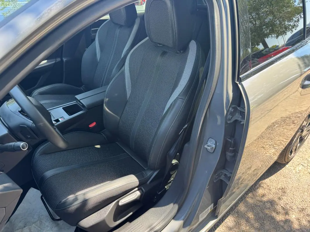 Vue intérieure côté conducteur d'une Peugeot 308 gris 2025, mettant en valeur le siège réglable en hauteur et l'accoudoir central.
