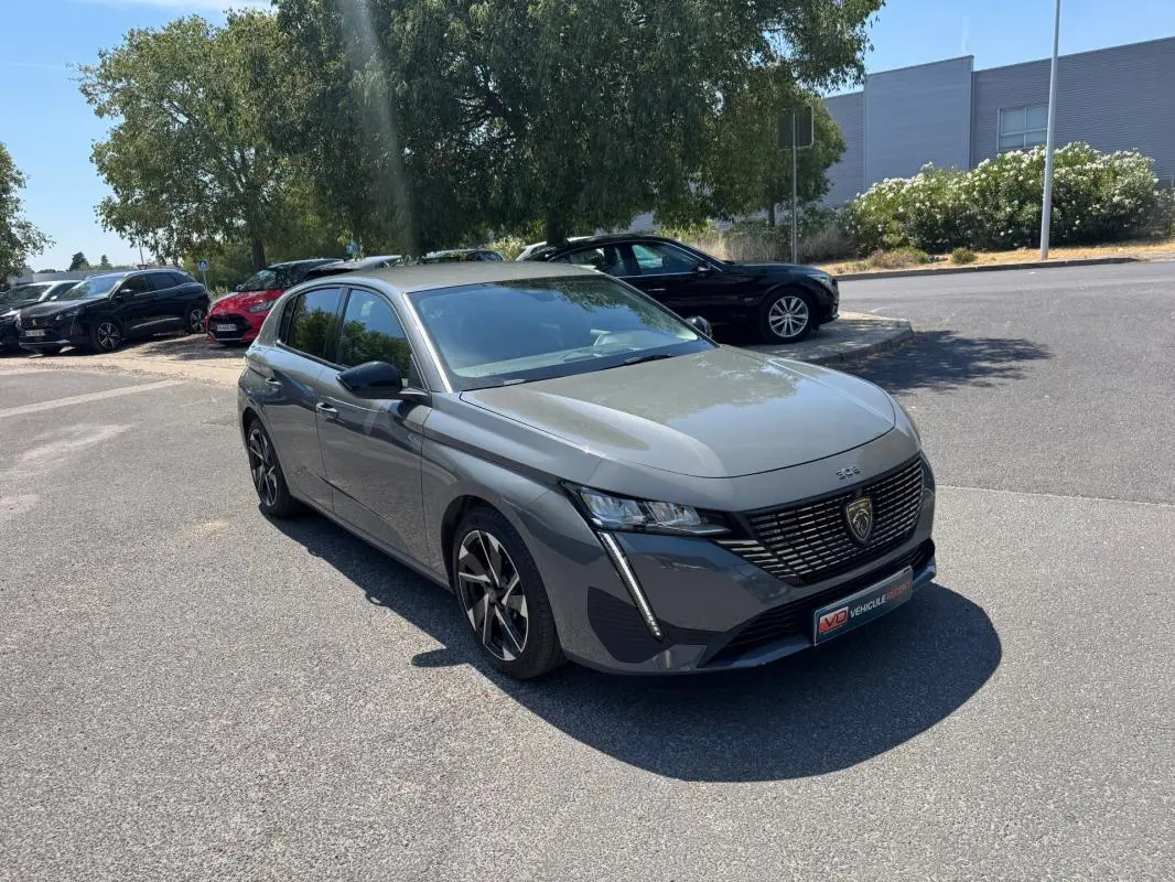 Peugeot 308 gris vue 3/4 avant droit, avec jantes alliage 17 pouces et calandre noire distinctive.