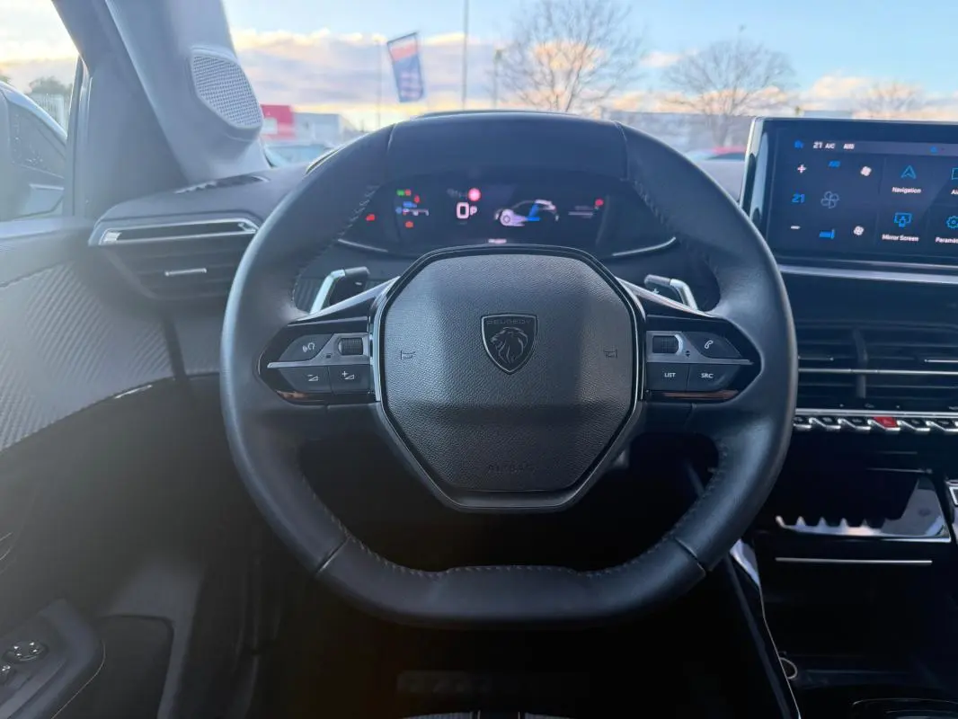 Vue intérieure centrée sur le volant noir de la Peugeot 208 Hybrid 110 e-DCS6 Allure avec tableau de bord numérique et écran tactile.