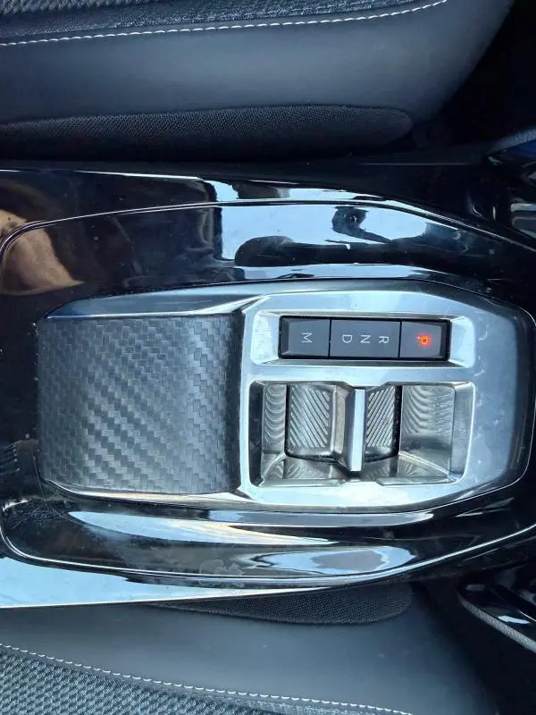 Vue plongeante sur la console centrale noire du Peugeot 208 Hybrid 110, avec levier de vitesses automatique et finition carbone.