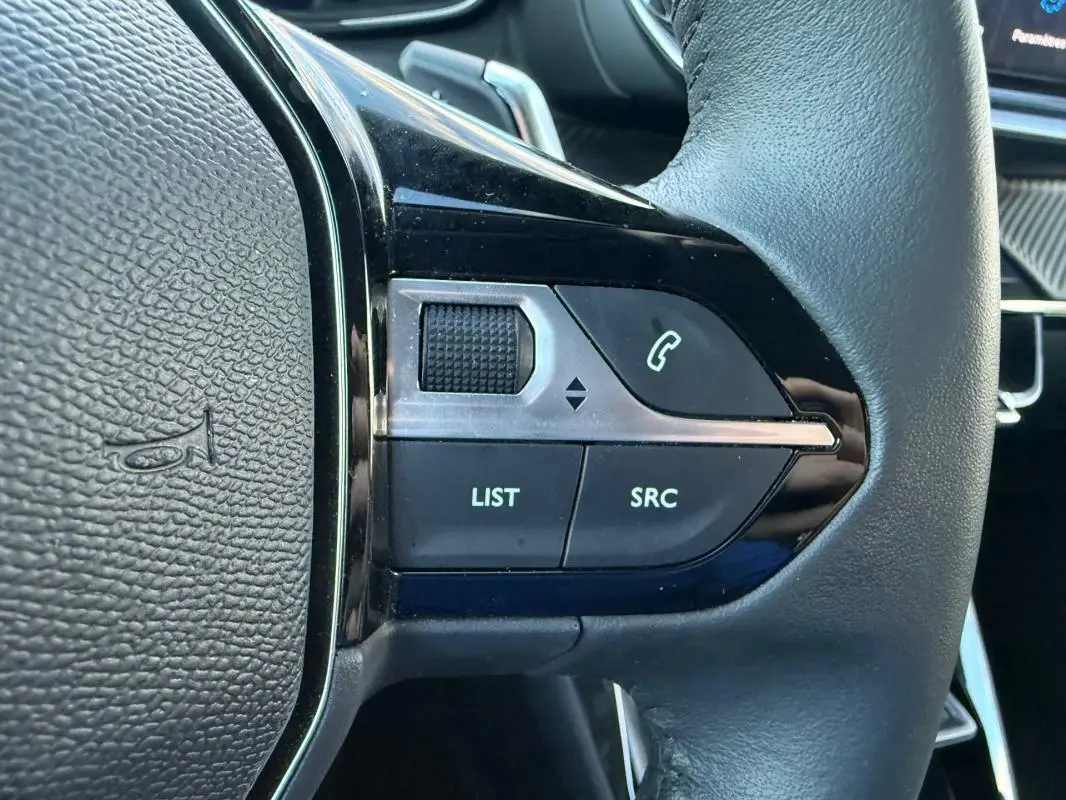 Gros plan sur les commandes gauche du volant noir du Peugeot 208 Hybrid 110 e-DCS6 Allure 2024, avec boutons Bluetooth et réglages.