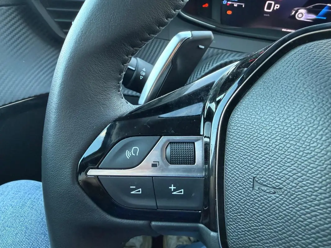Gros plan sur le côté gauche du volant noir de la Peugeot 208 Hybrid 110 e-DCS6 Allure avec commandes audio et régulateur.