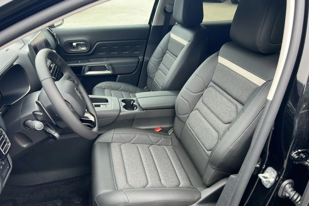 Intérieur avant du Citroën C5 Aircross Hybrid noir 2025, sièges tissu et cuir gris, volant multifonctions visible côté gauche.