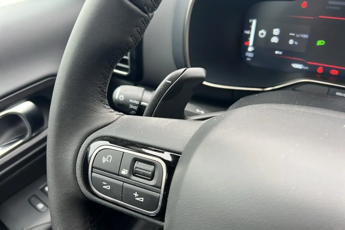 Gros plan sur le volant cuir noir du Citroën C5 Aircross Hybrid 145, avec commandes multifonctions et palettes au volant visibles.