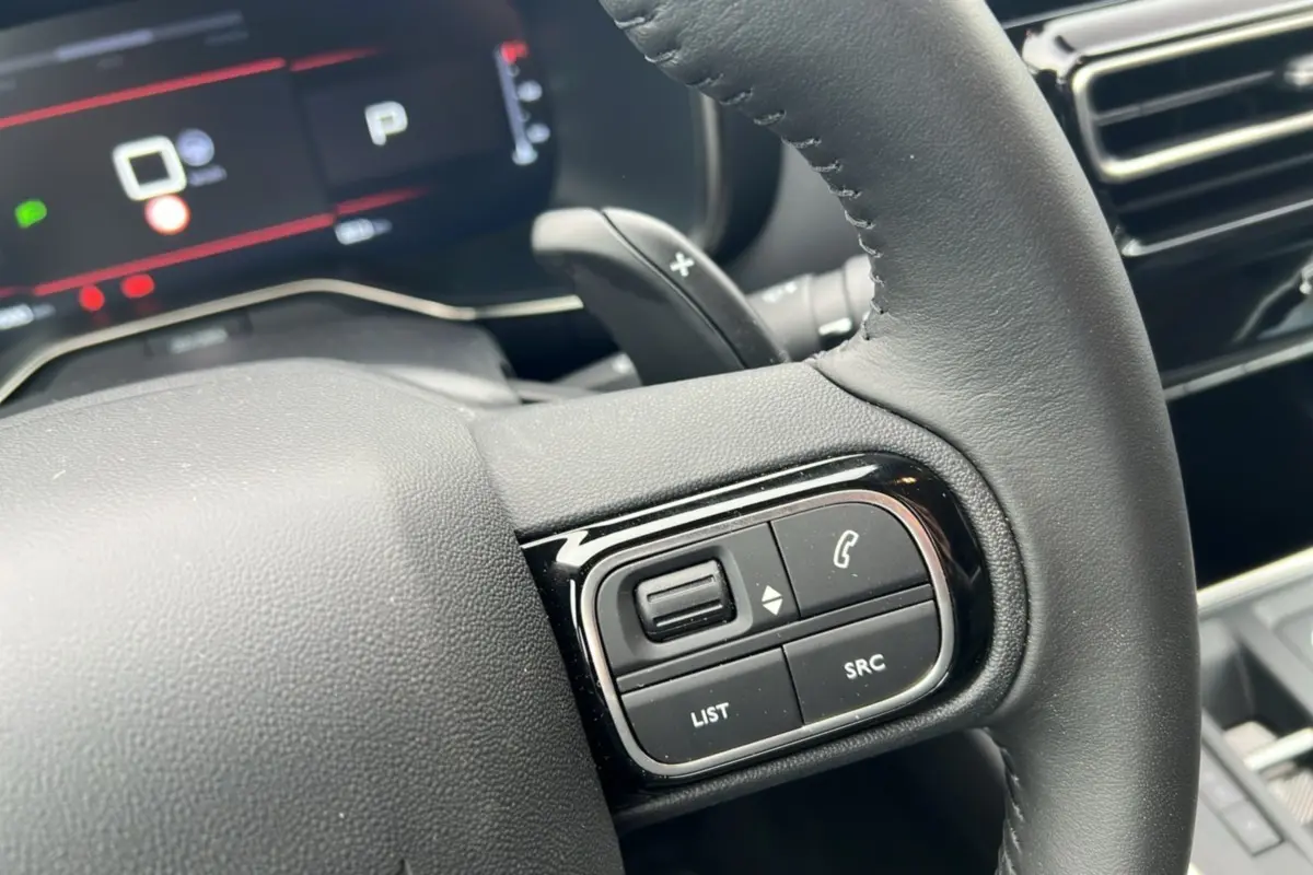 Gros plan sur le volant cuir noir du Citroën C5 Aircross Hybrid 145, avec commandes multifonctions et palettes au volant visibles.