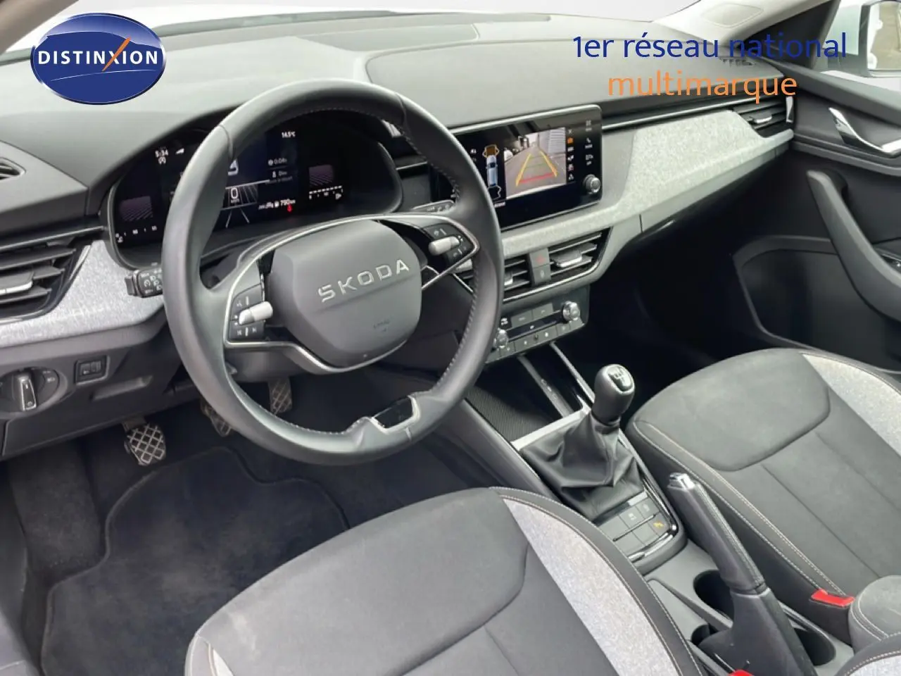 Vue intérieure de la Skoda Scala 2025 montrant le tableau de bord, volant cuir, écran central et sièges tissu gris noir.