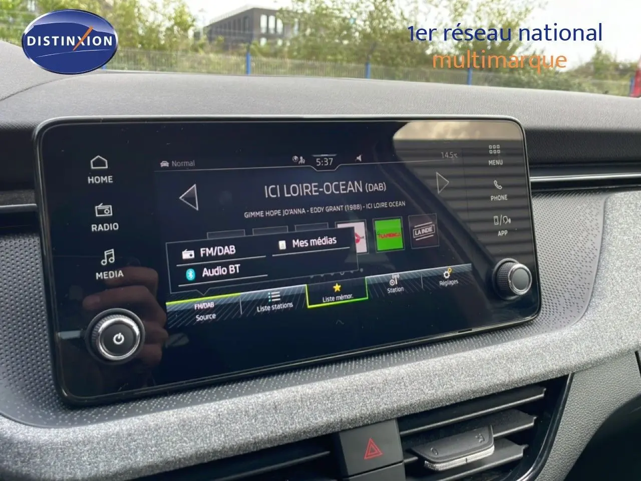 Écran tactile central du tableau de bord de la Skoda Scala blanc glacier, affichant la radio FM/DAB et Bluetooth.