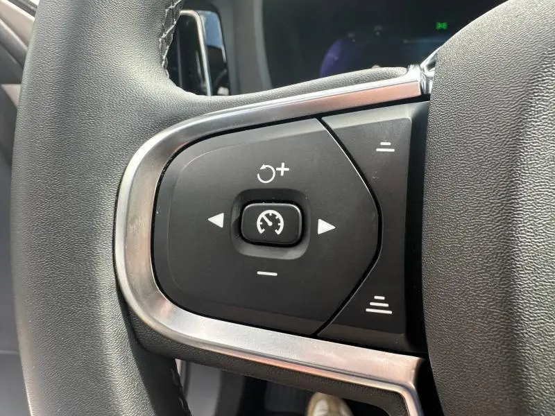 Gros plan sur les commandes de régulateur de vitesse au volant cuir du Volvo XC60 gris 2024 côté gauche.