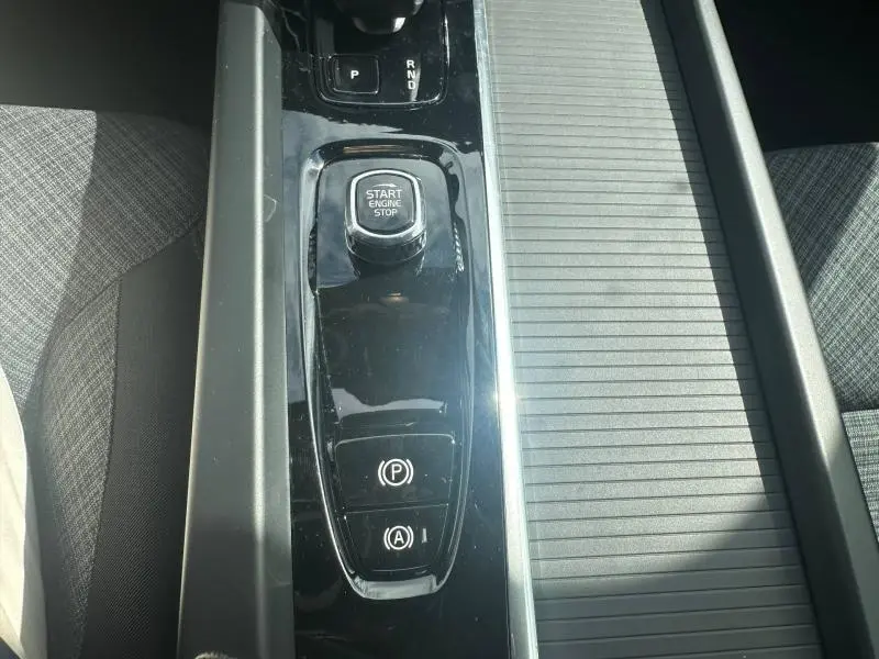 Vue rapprochée de la console centrale noire brillante du Volvo XC60 2024, avec bouton Start/Stop et commandes de frein.